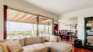 Una sala de estar moderna con un amplio sofá modular, una zona de comedor con sillas de madera y vistas al exterior.