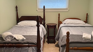A room with two wooden beds, a small wooden nightstand, a window with blinds, and an air conditioning unit on the wall. - Brimfield Waterfront cottage (Brimfield)