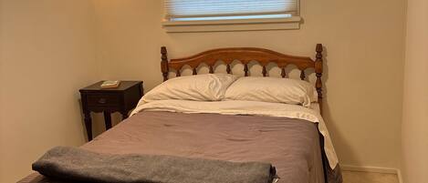 A bedroom with a wooden bed, a bedside table, a lamp, and a window with blinds.