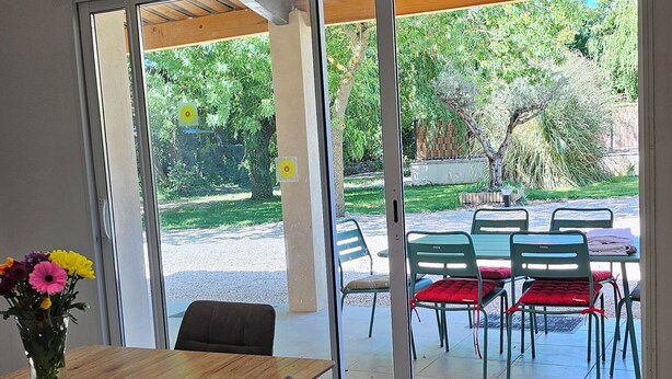 Ein moderner Essbereich mit Holztisch und -stühlen, einer Blumenvase und Blick auf eine Terrasse mit grünen Stühlen und einer Holzpergola.