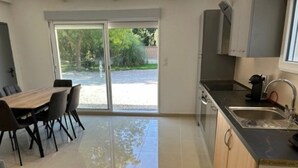 Eine moderne Küche mit großem Fenster, einem Essbereich mit Tisch und Stühlen sowie Blick auf einen Garten.