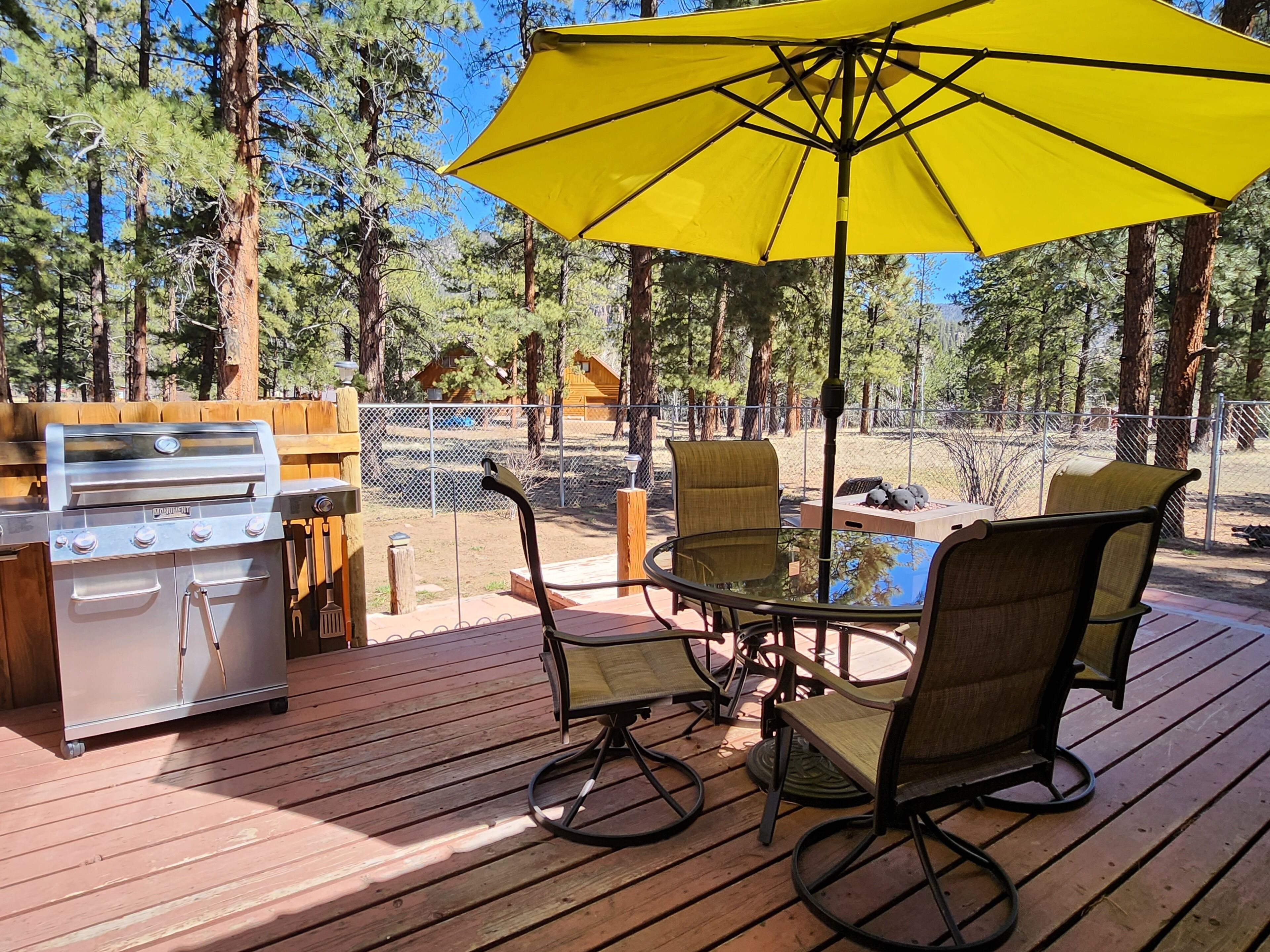 Une terrasse extérieure avec un barbecue, des chaises et un parasol jaune.