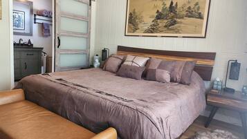 A bedroom with a large bed, a bench, a dresser, a mirror, and a painting on the wall.