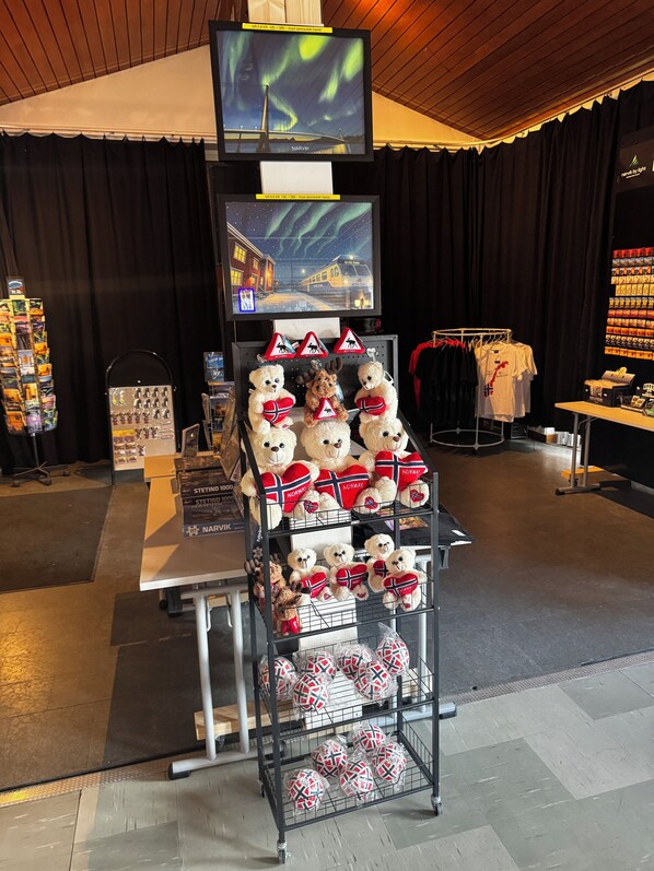 A display of merchandise including stuffed animals and souvenirs, with a television above showing the aurora borealis. - Sjømannskirken Hostel (Narvik)