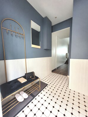 Ein Hotelzimmer mit einem schwarz-weißen Fliesenboden, einem schwarzen Sofa mit einer gesteppten Tasche, einem goldfarbenen Metallgestell und einem Spiegel an der Wand.