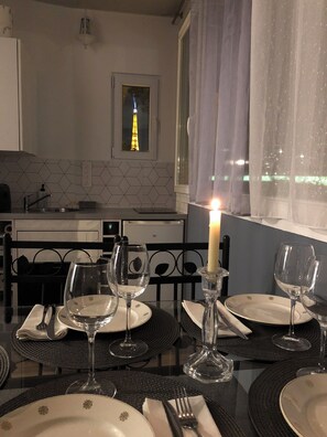 A dining table set with plates, glasses, and cutlery, a lit candle, and a view of the Eiffel Tower through a window. - Loft Avec vue sur la Tour Eiffel et sur la Seine (Paris)