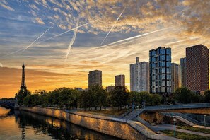 Paesaggio urbano con moderni grattacieli, un fiume e la Torre Eiffel sullo sfondo.