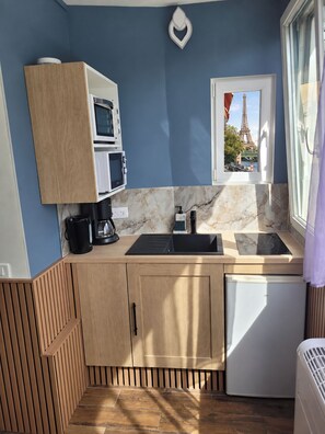 Una cocina compacta con horno integrado, microondas y vista a la Torre Eiffel a través de una ventana.