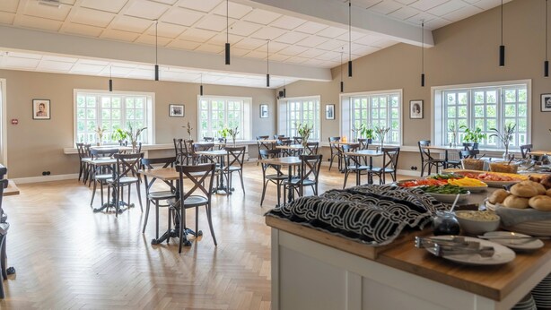 A spacious dining area with multiple tables and chairs, large windows with natural light, and a buffet with various food items. - Hotel Stafholt (Borgarbyggd)