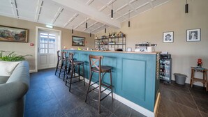 A bar area with stools, a counter, and a refrigerator stocked with bottles. - Hotel Stafholt (Borgarbyggd)