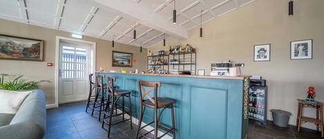 A bar area with stools, a counter, and a refrigerator stocked with bottles.