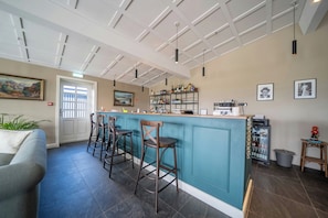 Zona de bar con taburetes, una barra y un refrigerador lleno de botellas.