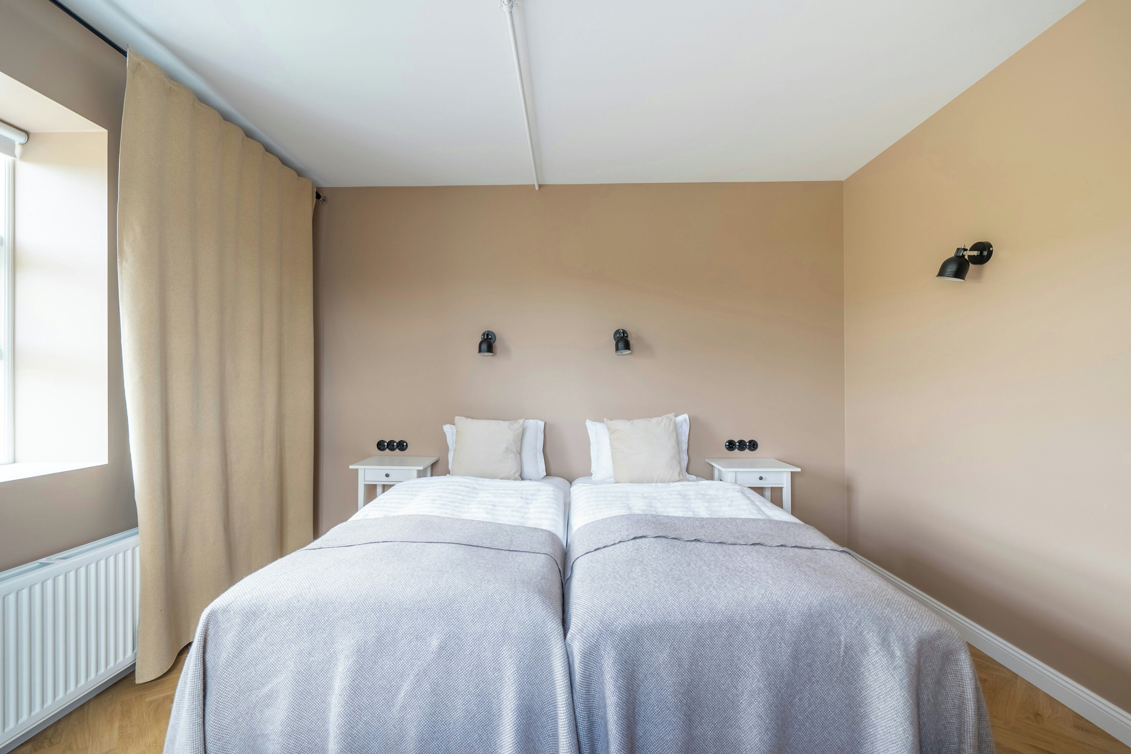 A double bed with two nightstands, a window with curtains, and a wall-mounted light fixture.