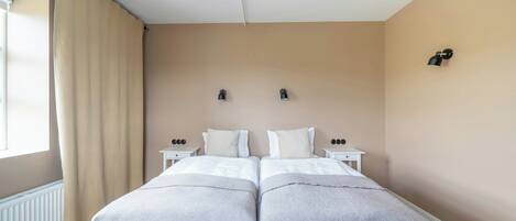 A double bed with two nightstands, a window with curtains, and a wall-mounted light fixture.