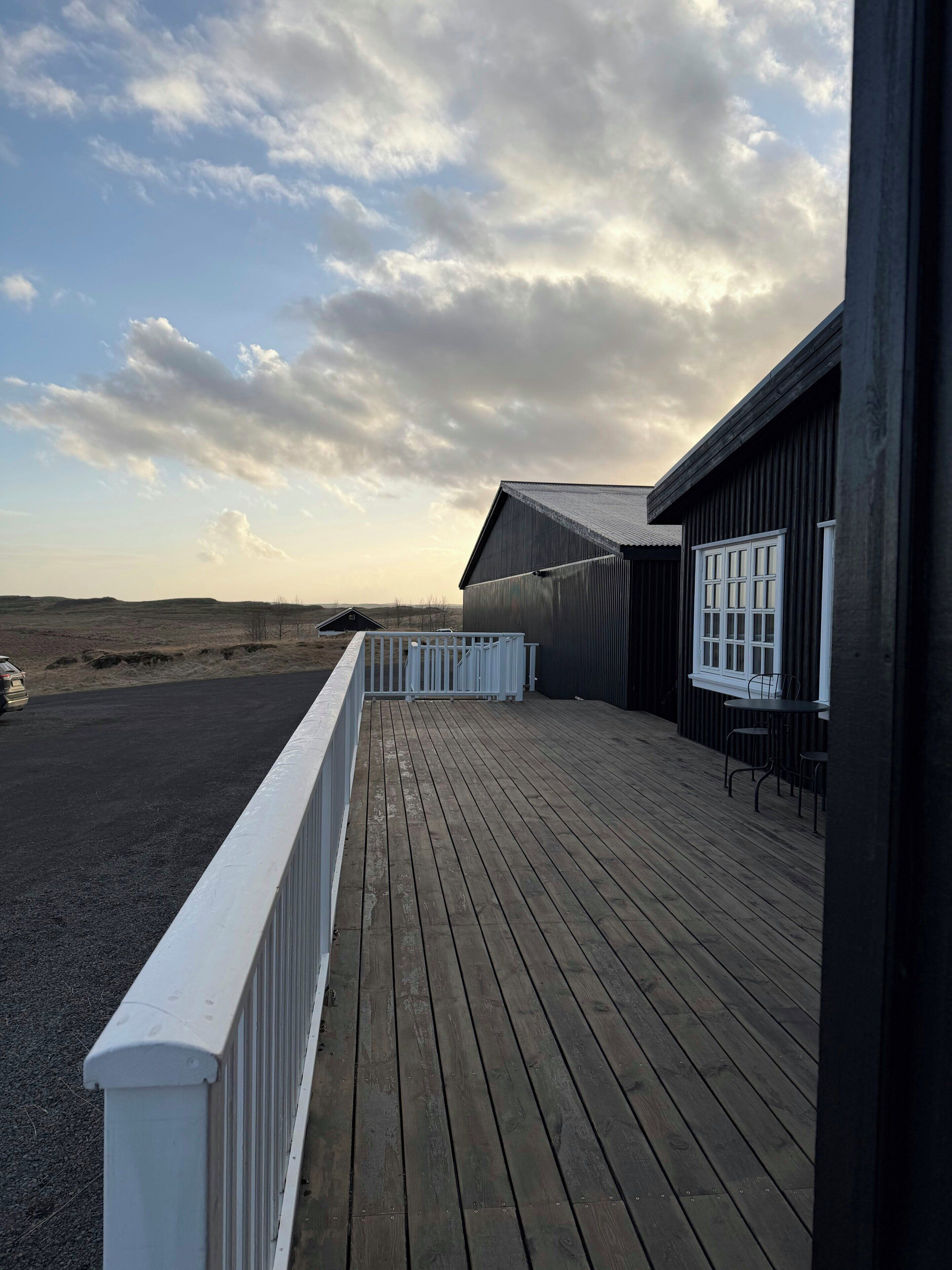 A wooden deck with a white railing, a building with a dark exterior, and a view of the landscape.