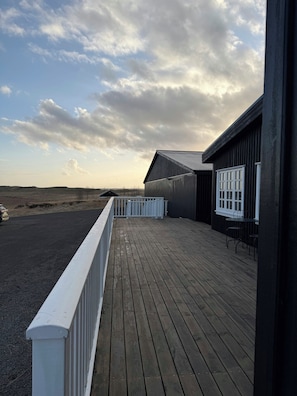 A wooden deck with a white railing, a building with a dark exterior, and a view of the landscape. - Hotel Stafholt (Borgarbyggd)