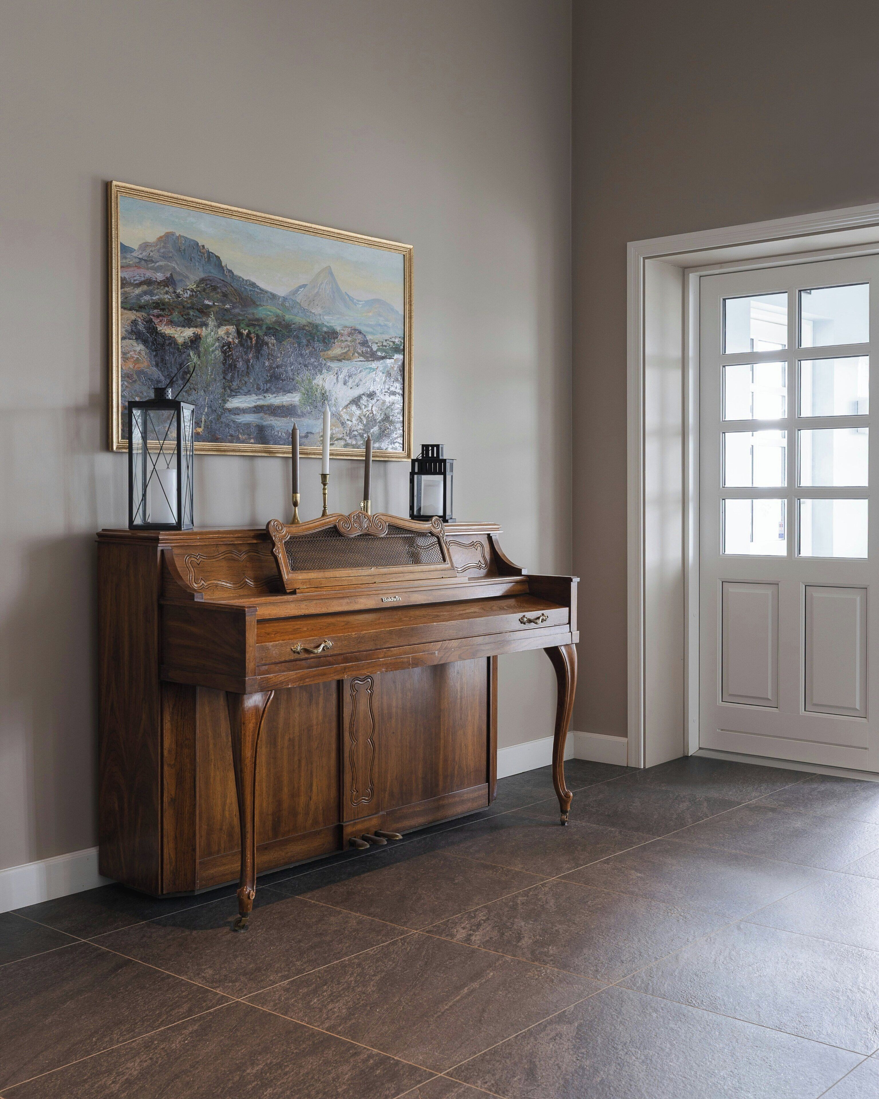 A wooden console table with a painting above it, a door with a window, and a tiled floor.