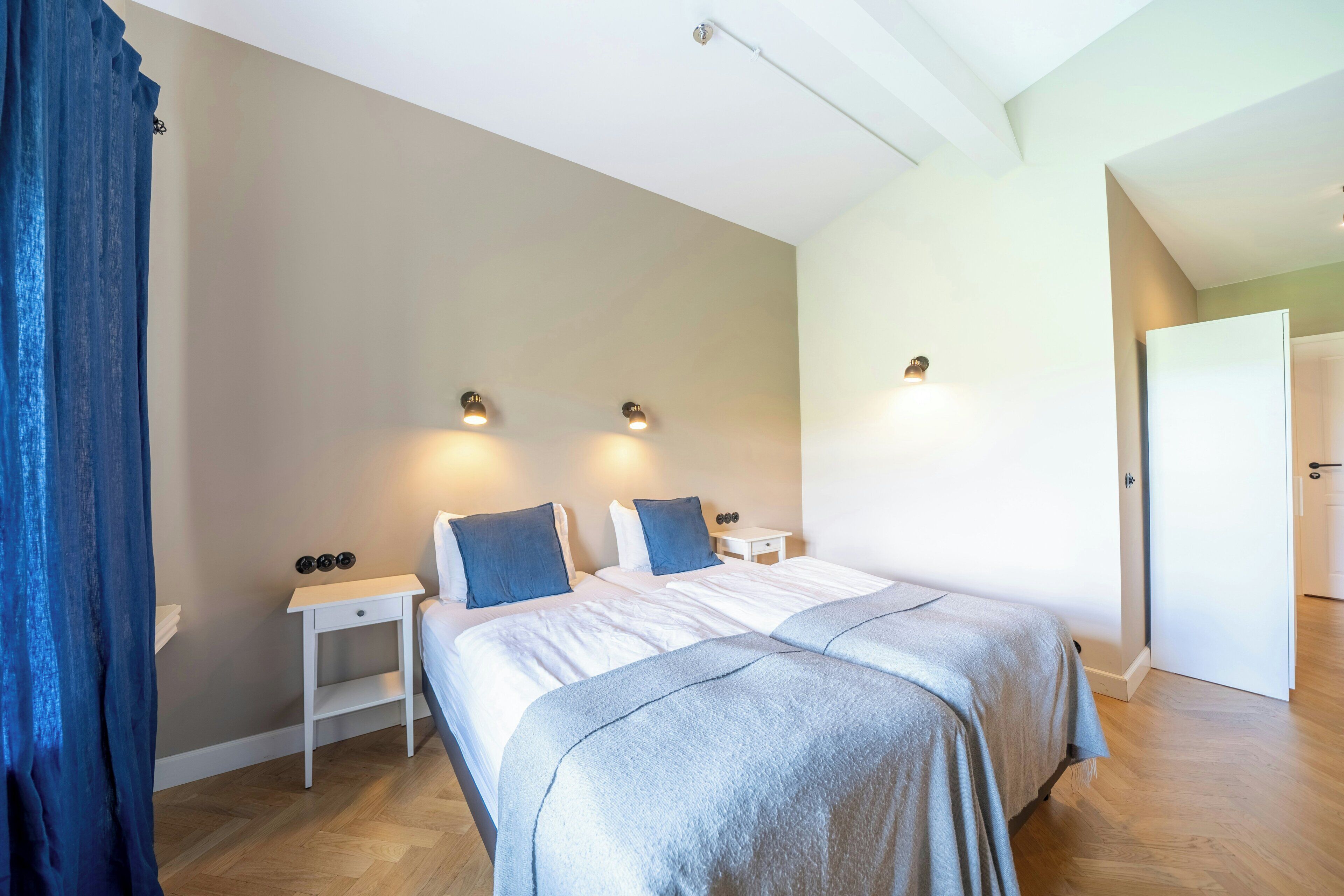 A bedroom with two beds, a bedside table, a nightstand, and a door to another room.