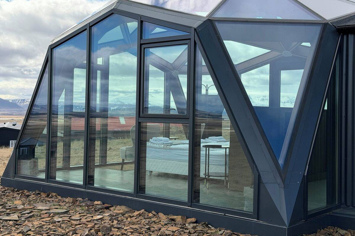Eine moderne Geodätengewächshauskonstruktion mit großen Glasflächen, einem Betonfundament und Blick auf eine gebirgige Landschaft.