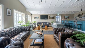 A modern living room with leather sofas, a coffee table, and a bar area with stools. - Hotel Stafholt (Borgarbyggd)
