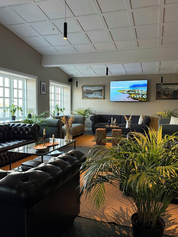 A spacious living room with a large window, a flat-screen TV, and multiple sofas. - Hotel Stafholt (Borgarbyggd)