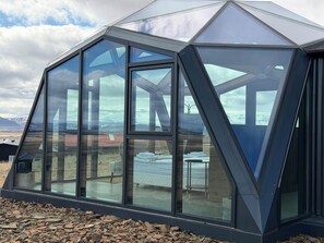 A modern geodesic greenhouse structure with large glass panels, a concrete foundation, and a view of a mountainous landscape. - Hotel Stafholt (Borgarbyggd)
