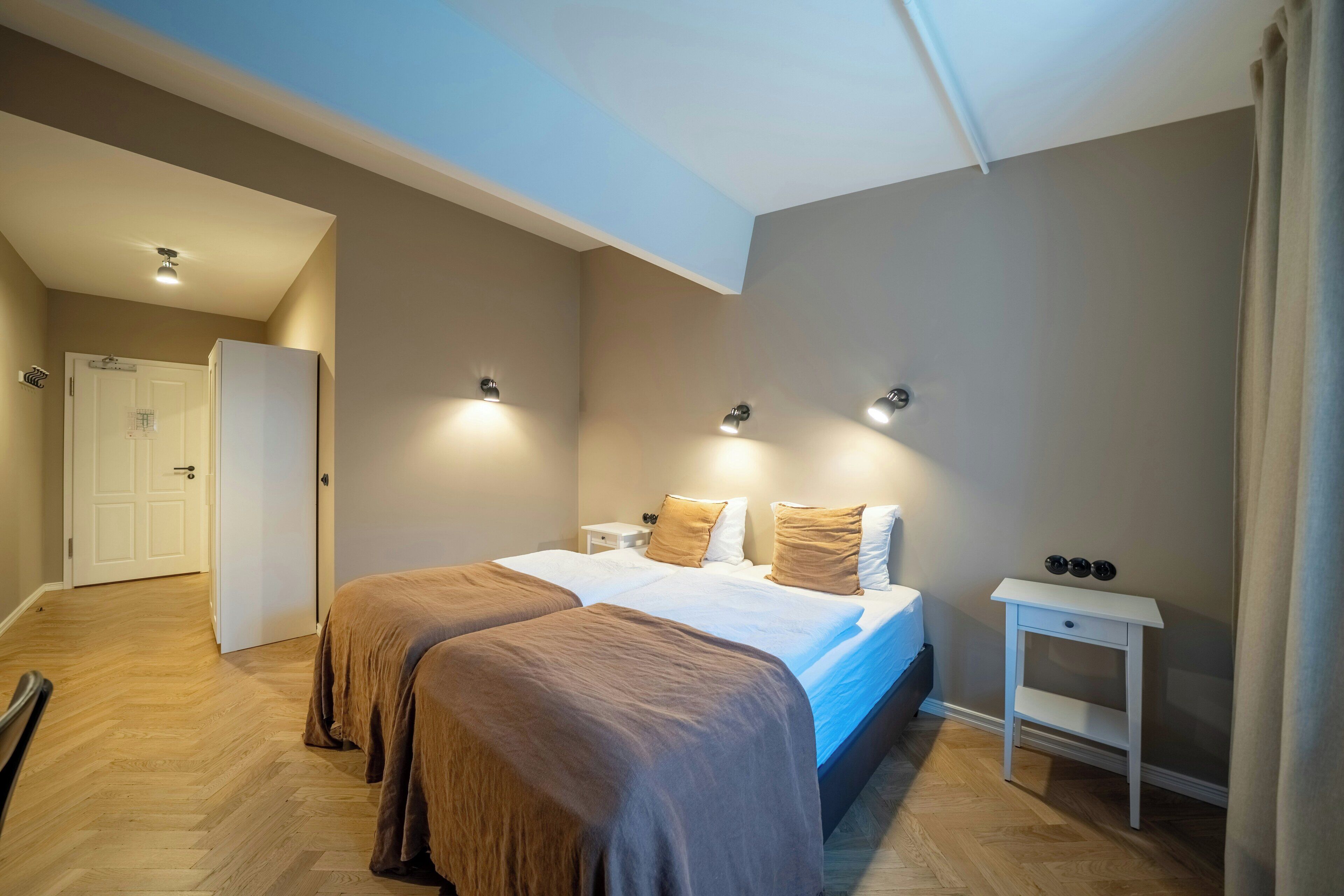 Une chambre avec deux lits, une table de chevet, une petite table, une porte et un luminaire au plafond.