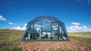 A geodesic dome structure with a glass facade, set on a rocky terrain with a clear sky. - Hotel Stafholt (Borgarbyggd)