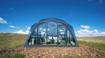 Estructura en forma de cúpula geodésica con fachada de vidrio, ubicada sobre terreno rocoso bajo un cielo despejado.