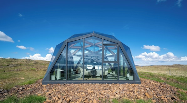 Estructura en forma de cúpula geodésica con fachada de vidrio, ubicada sobre terreno rocoso bajo un cielo despejado.