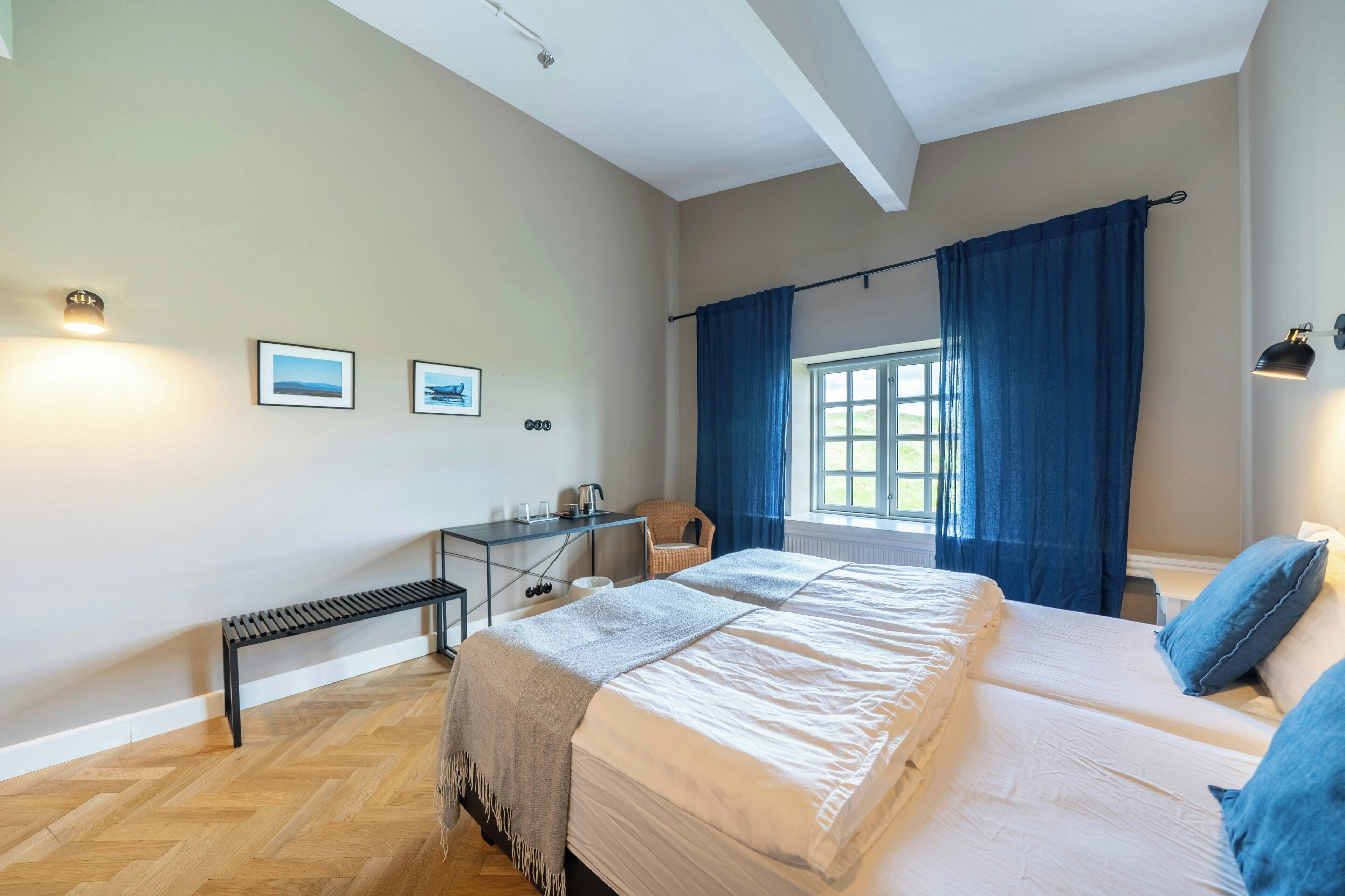 A bedroom with a large bed, a desk with a chair, a bench, and a window with curtains.