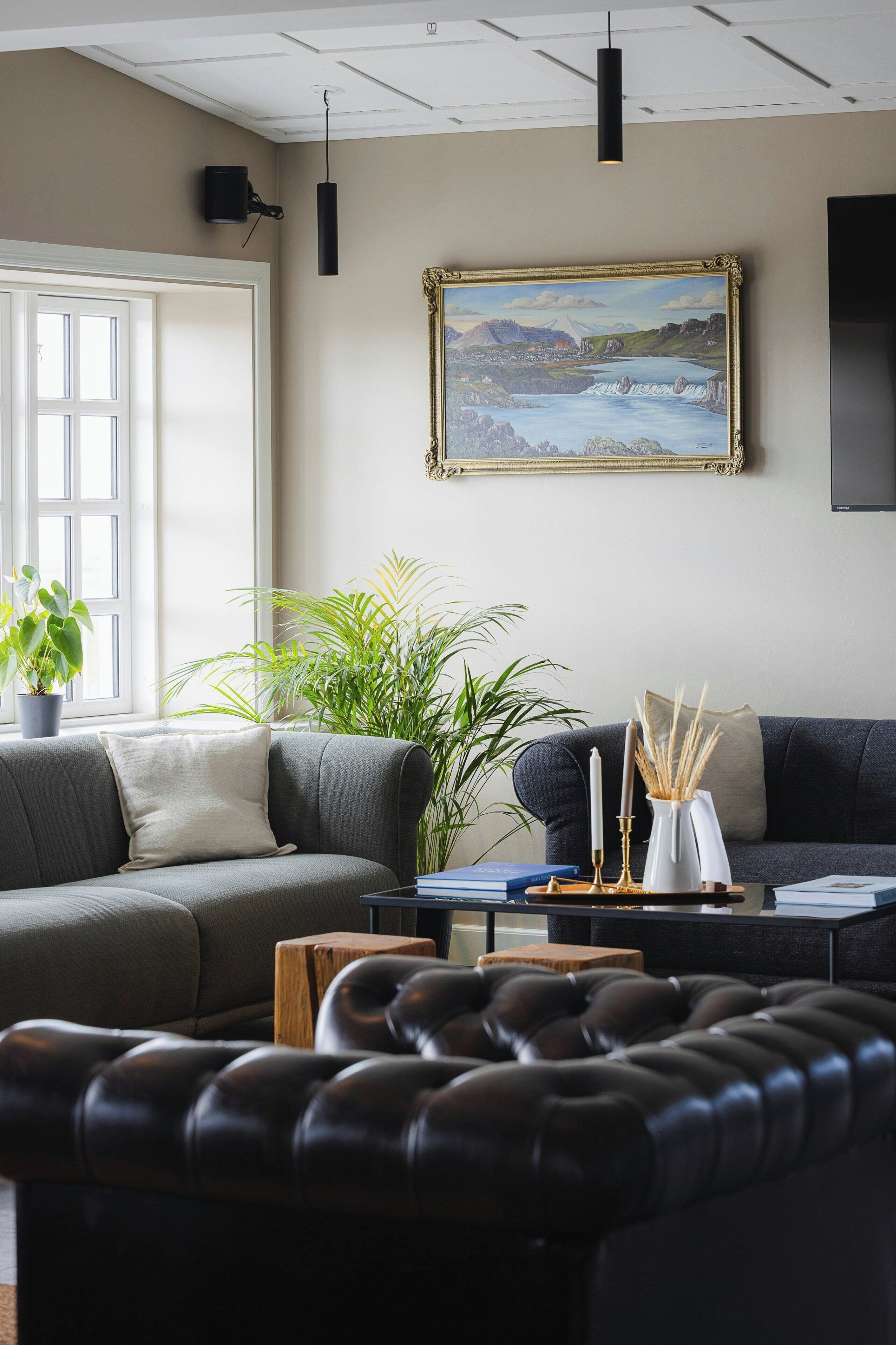 A modern living room with a sectional sofa, a leather ottoman, a coffee table, and a large landscape painting on the wall.