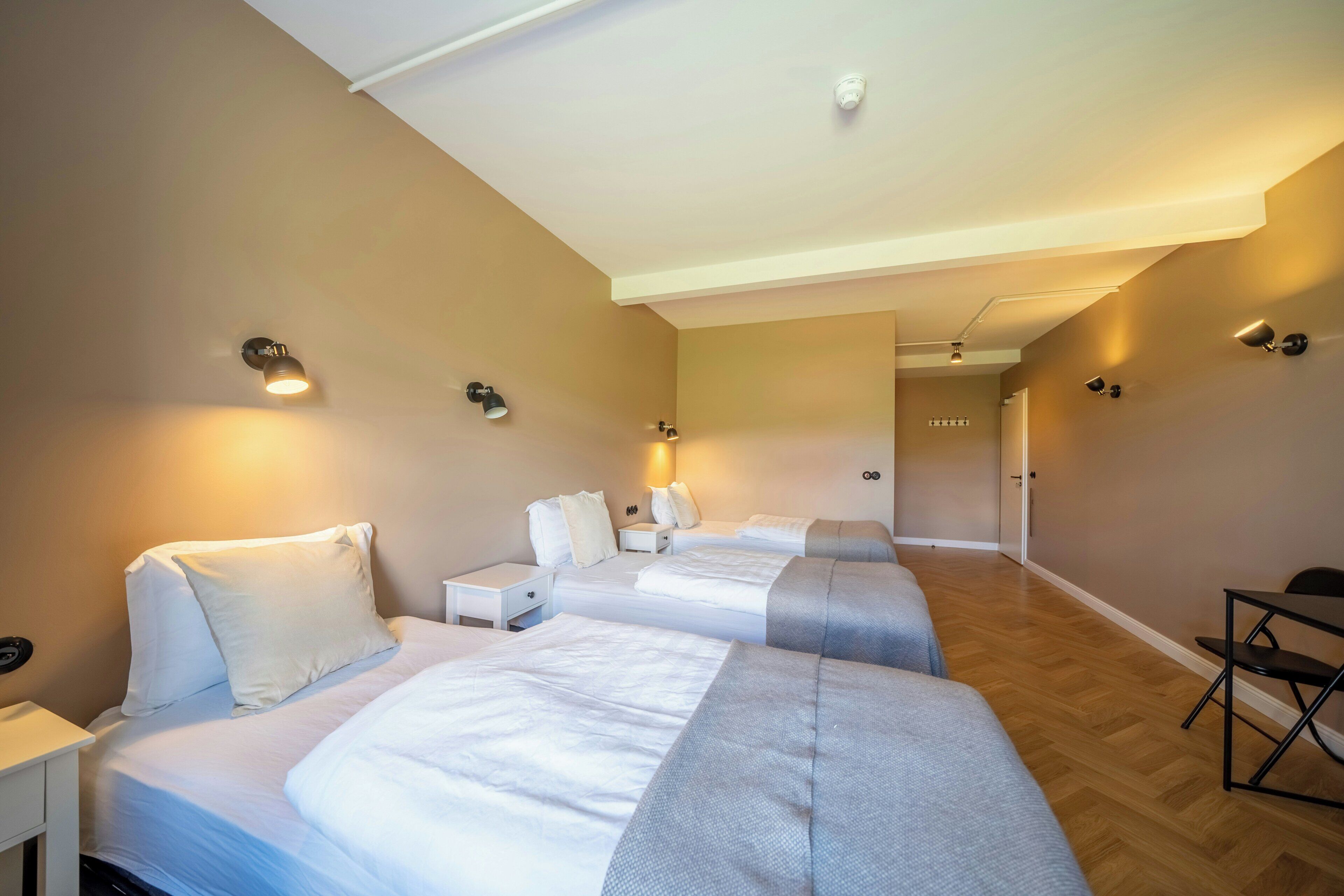 Et hotelværelse med tre senge, et skrivebord og en stol.