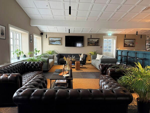 A modern lounge area with leather sofas, a coffee table, and a bar area with stools. - Hotel Stafholt (Borgarbyggd)
