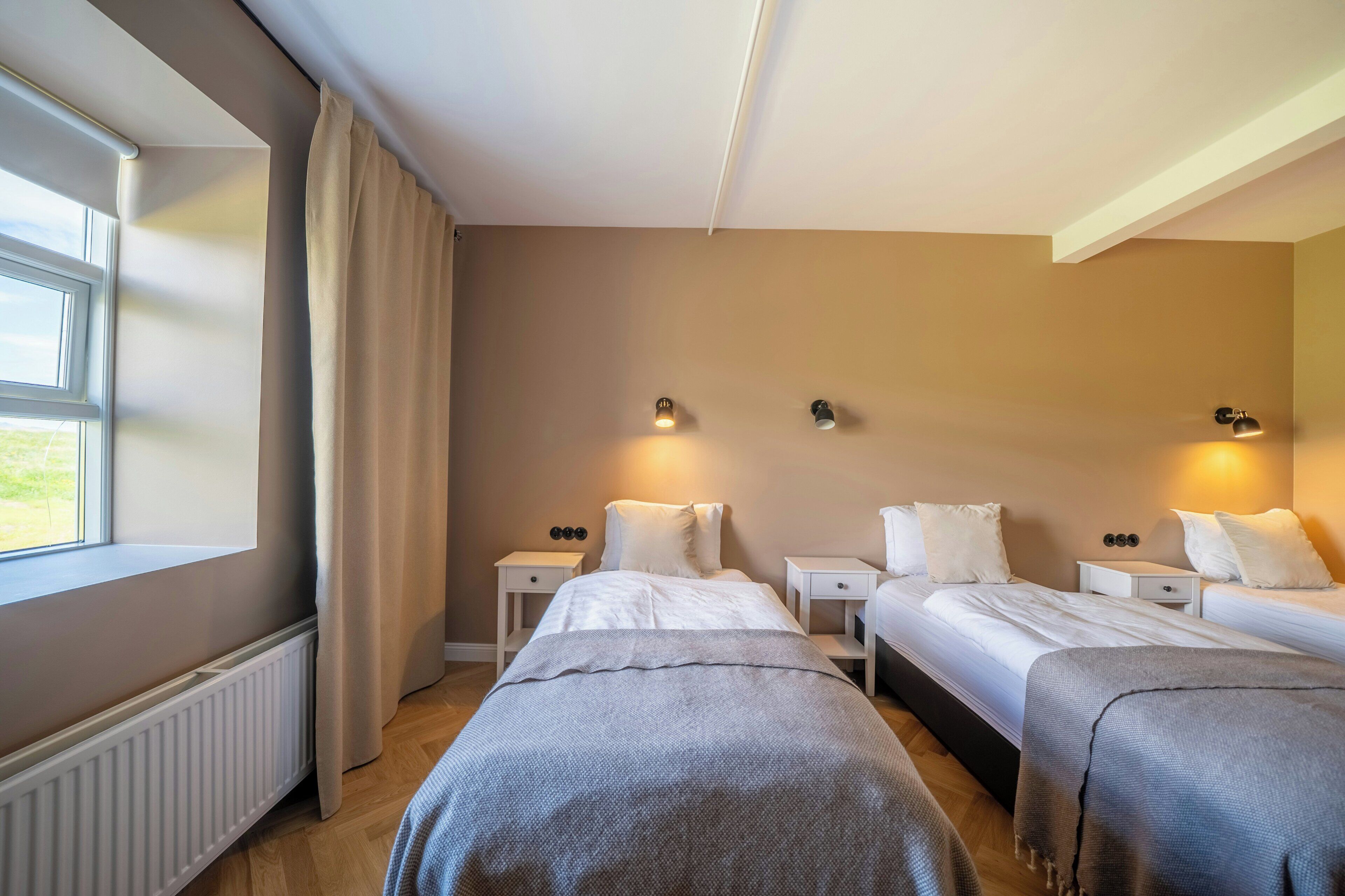 Een hotelkamer met twee bedden, een raam, een radiator en wandlampen.