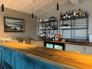 A bar area with shelves of liquor bottles, glasses, and a painting on the wall. - Hotel Stafholt (Borgarbyggd)