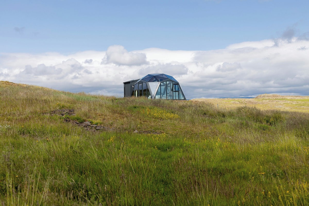 A modern glass structure in a grassy field with a clear sky.