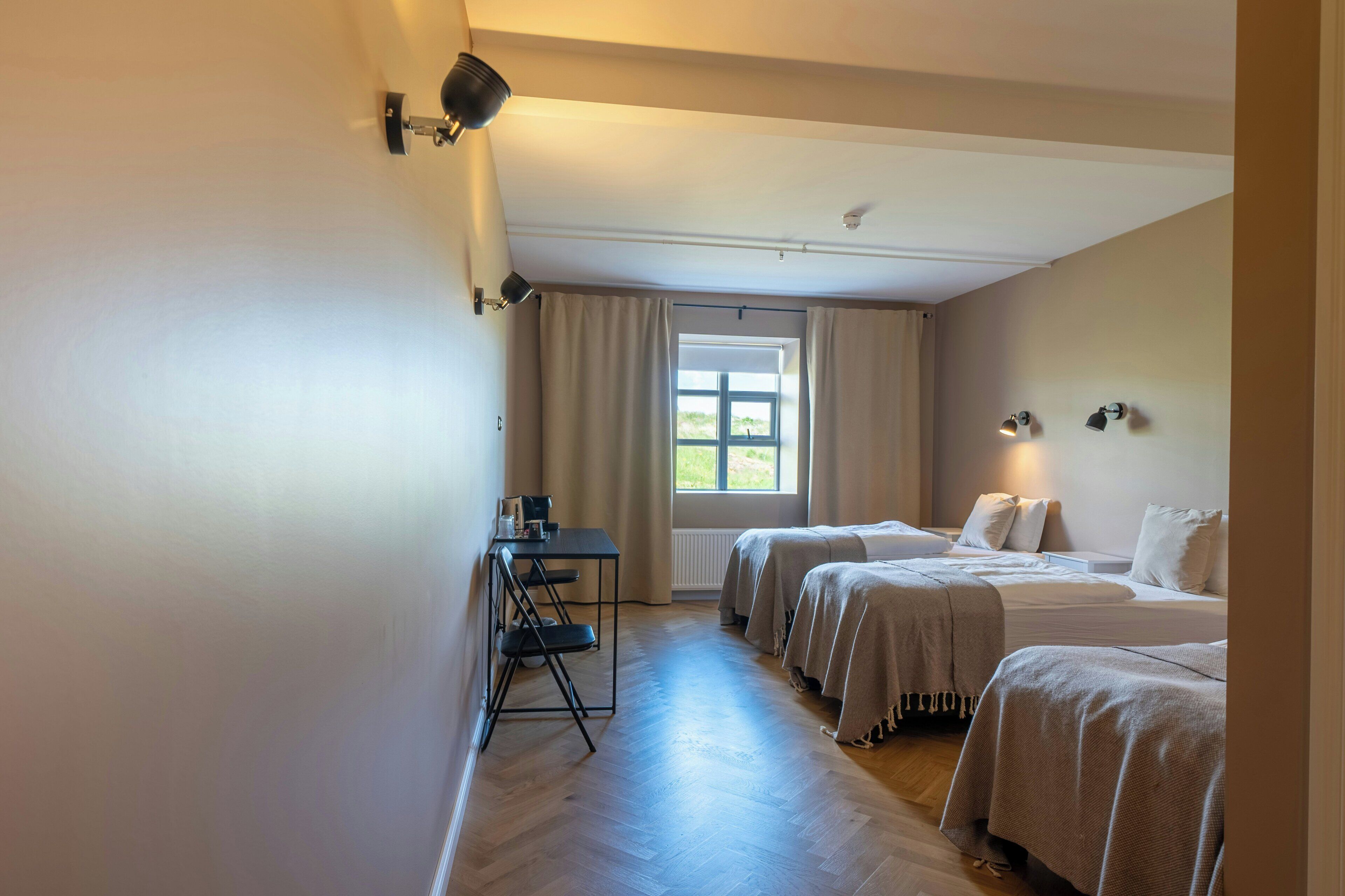A hotel room with two beds, a desk, and a window with curtains.