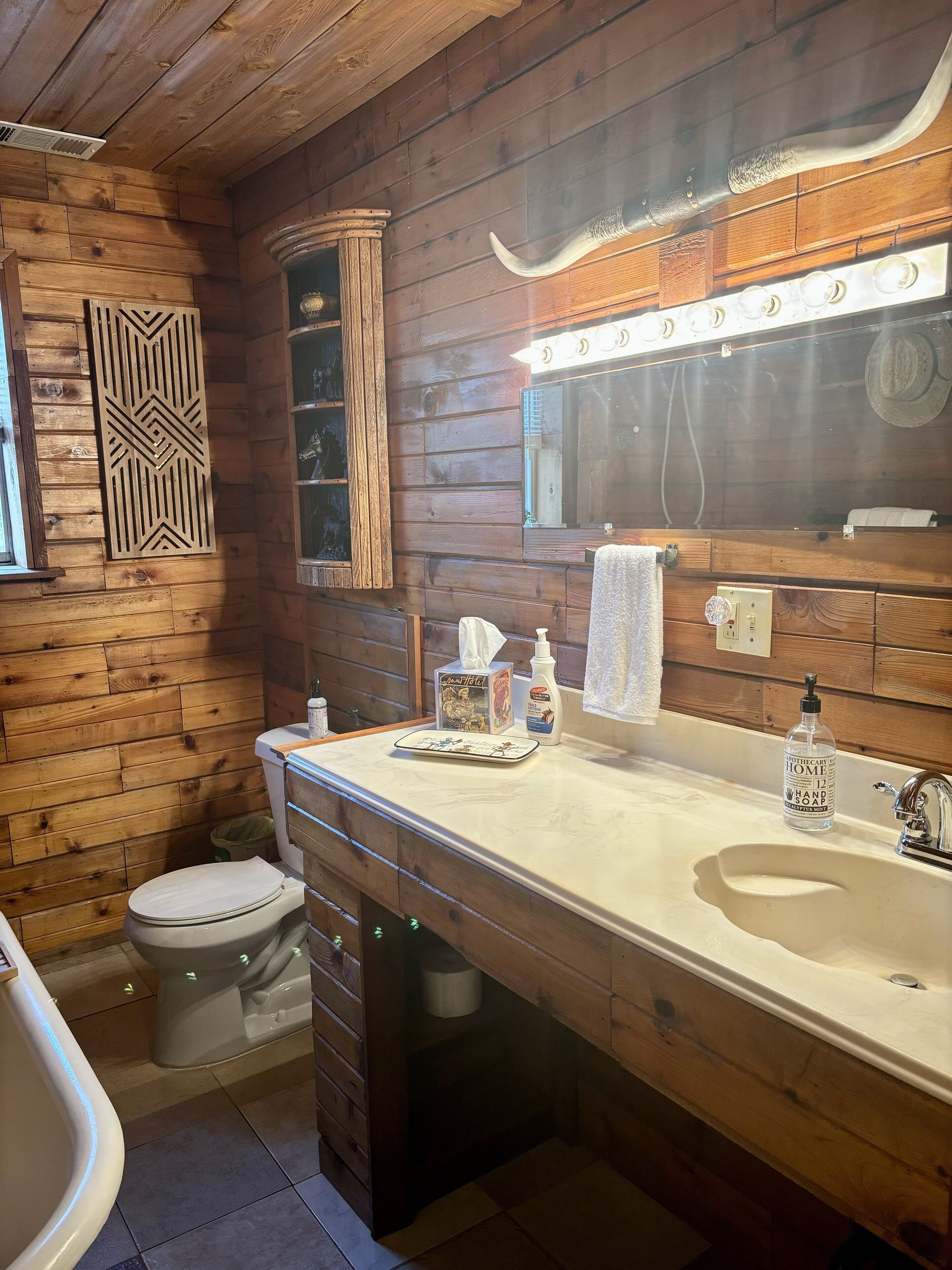 A wooden cabin bathroom with a large mirror, vanity, and a toilet.