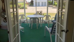A patio area with a table and chairs, a view of a parking lot, and a building in the background. - Cozy beach cottage. Less than a 2minute walk to the beach.  (Westbrook)