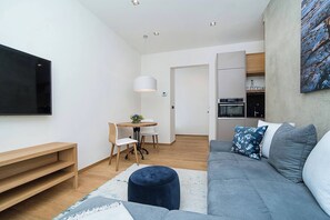 A modern living room with a grey sofa, a small round table, and a TV mounted on the wall. - Charming Apartment In Famous Area (Prague)