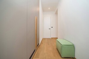 A hallway with a wooden floor, a green bench, and a white door at the end.