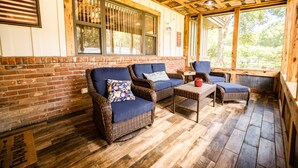 A covered patio area with wicker furniture, a brick wall, and large windows.