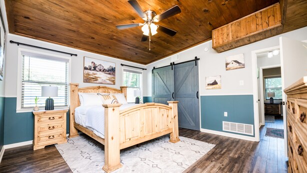 A bedroom with a wooden bed, a ceiling fan, a dresser, and a large window.