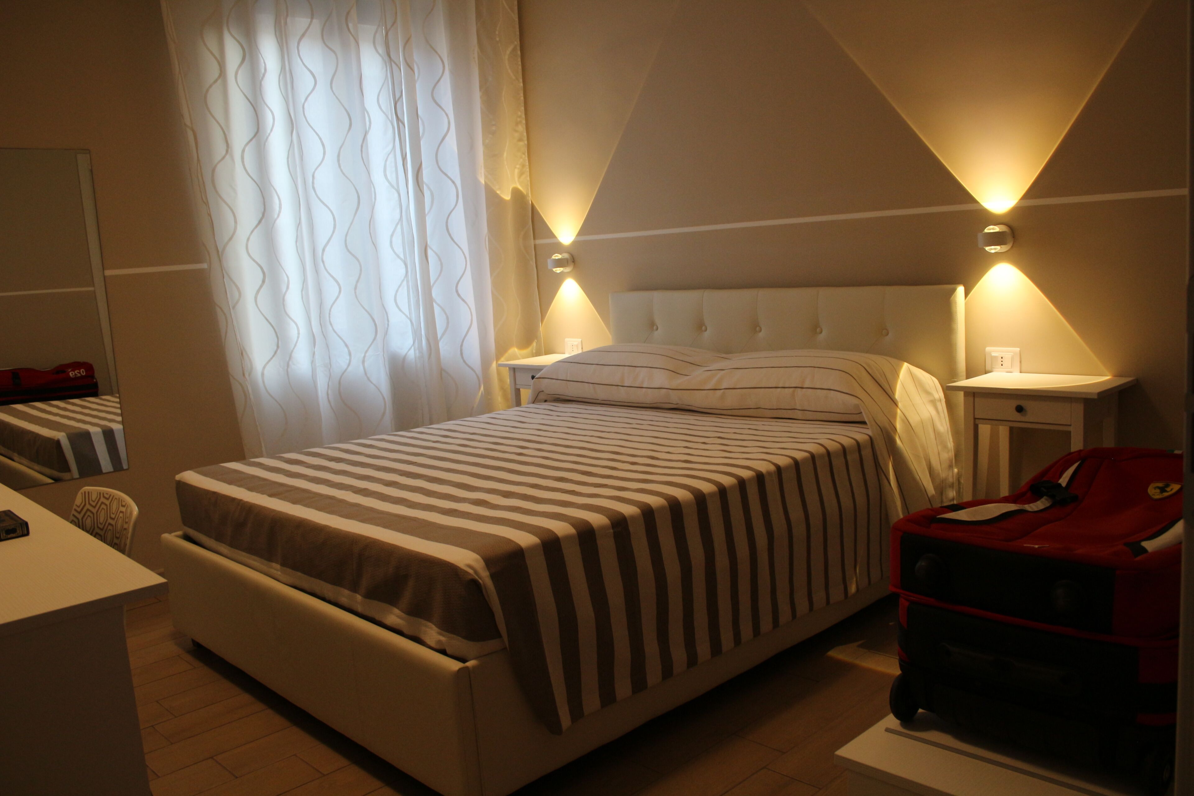 Ett hotellrum med en stor säng, sängbord, ett skrivbord och en röd resväska.