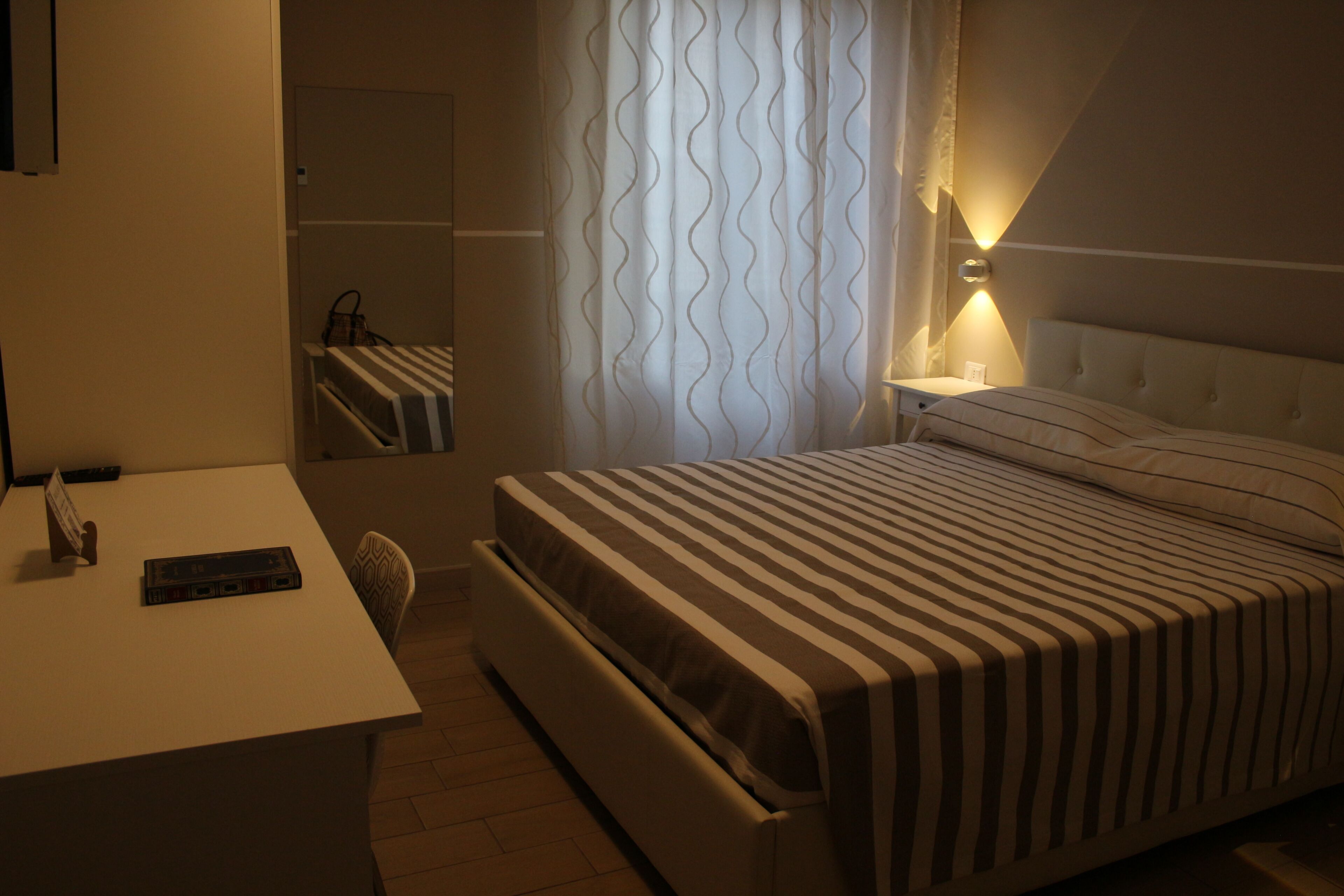 Una habitación de hotel con cama, mesita de noche, lámpara y espejo.