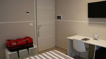 Une chambre d’hôtel avec un lit, un bureau et une chaise, une télévision et une valise rouge.
