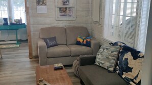 A cozy living room with a sofa set, a coffee table, and a wall-mounted air conditioner. - Bigfoot themed cottage.  Dog friendly! (Harrison)