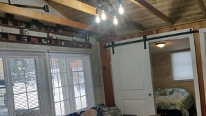 A cozy room with a wooden ceiling, a sofa, a small table, and a bed with a patterned bedspread. - Bigfoot themed cottage.  Dog friendly! (Harrison)