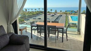 A balcony with a table and chairs, overlooking a parking area and a pool.